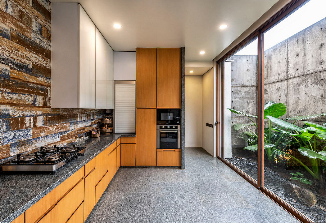 Modern kitchen with wood cabinetry, stone countertops, and concrete walls overlooking greenery.
