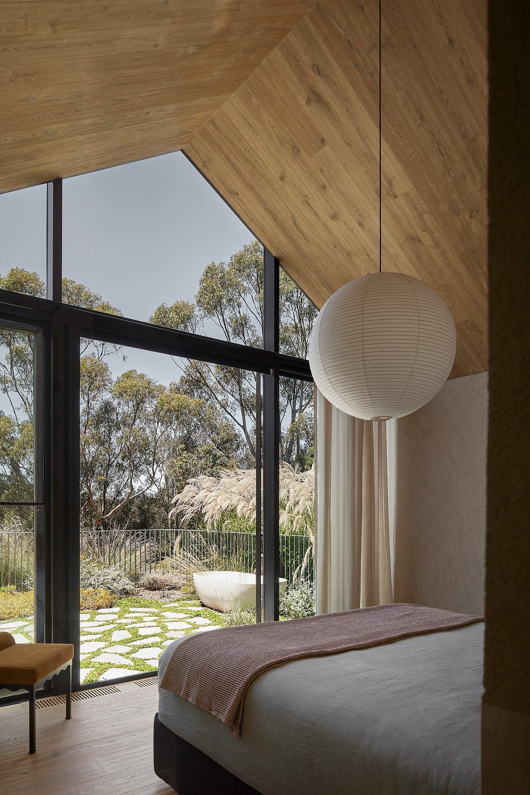 A room with a wooden ceiling and a large window overlooking a lush outdoor landscape, featuring a white pendant lamp.