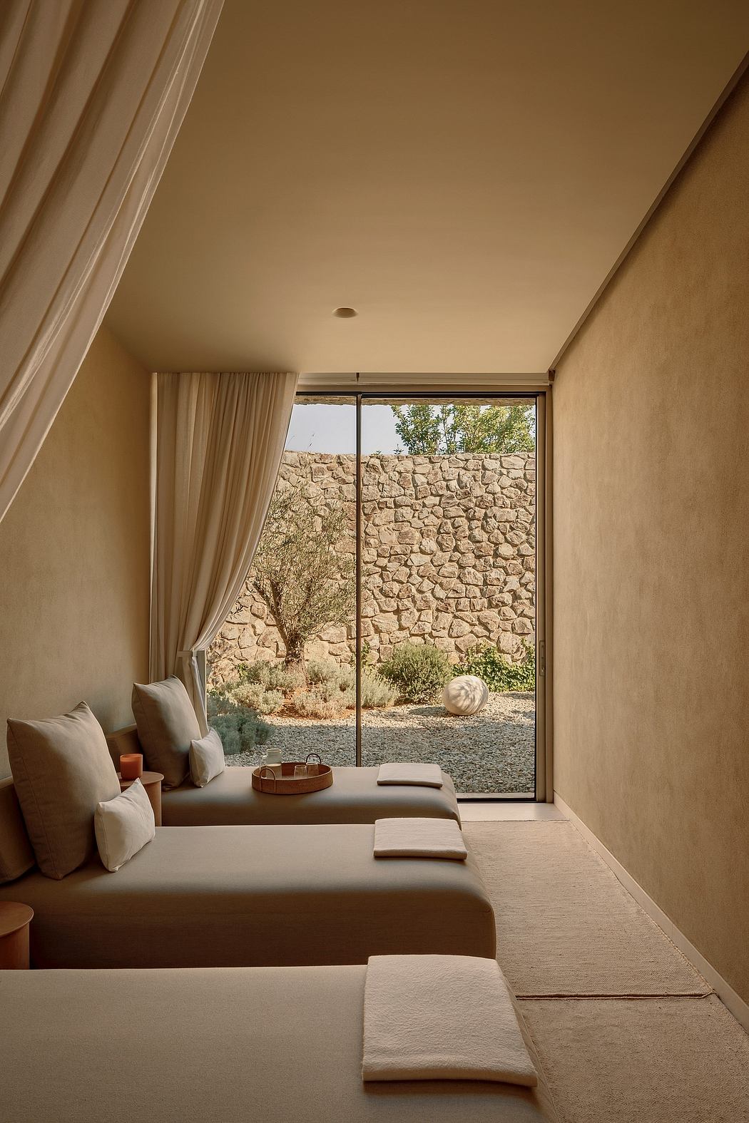 Serene desert-inspired interior with stone-clad walls, minimalist furnishings, and large window offering scenic view.