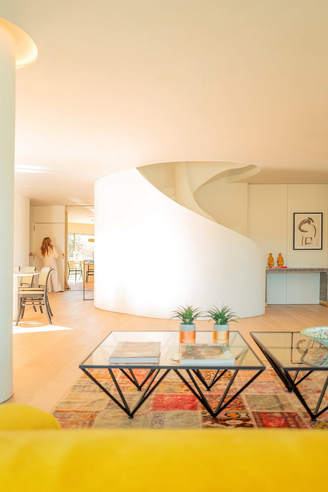 Minimalist interior with curved white wall, modern glass tables, and vibrant decor.