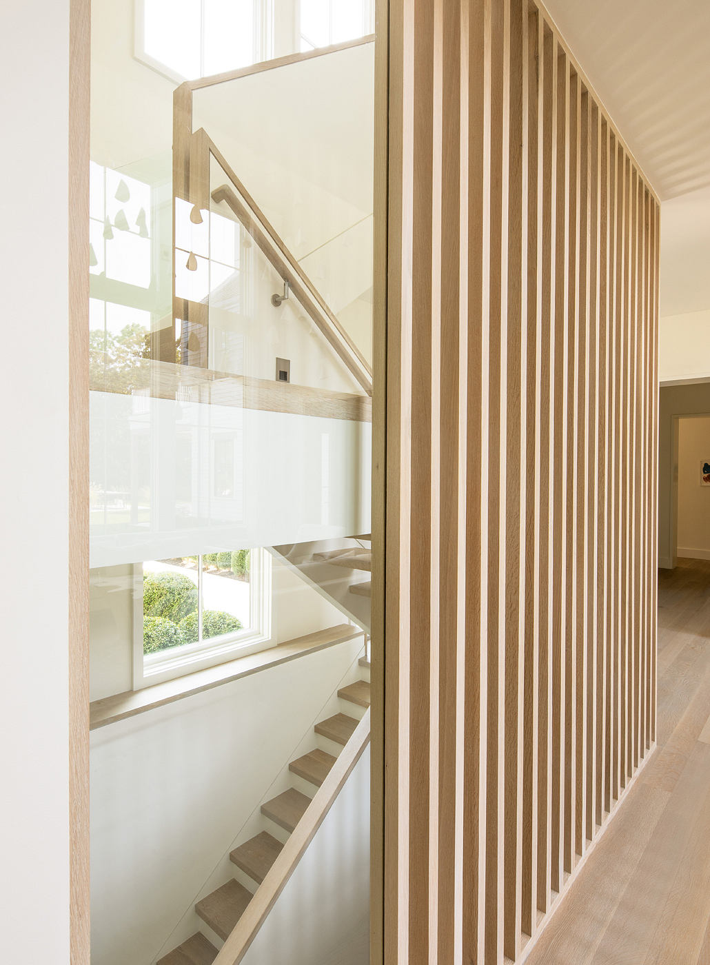 Elegant wooden staircase with minimalist railing design and large windows.