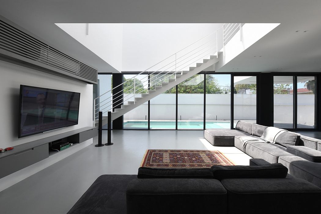 Sleek, modern interior with minimalist staircase, wall-to-wall windows, and a swimming pool visible.