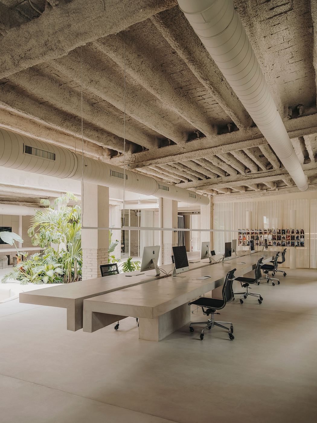 An open-concept office space with exposed concrete ceilings, minimalist desks, and lush greenery.