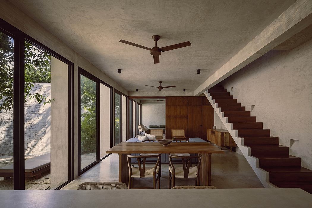 A cozy, modern interior with concrete walls, wood furniture, and a central staircase.