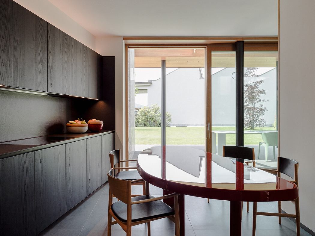 The image depicts a modern kitchen and dining area with wood-paneled walls, large windows, and a curved dining table.