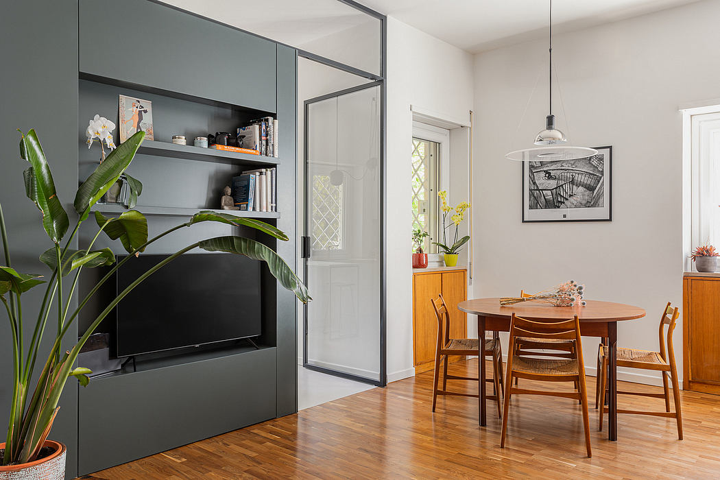 Modern, minimalist living room with gray built-in shelves, wooden dining table, and tropical plants.