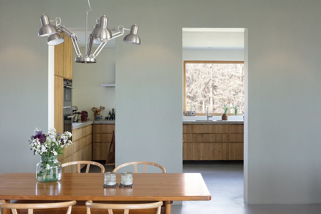 Modern, minimalist kitchen with wooden cabinetry, pendant lighting, and a large window overlooking natural scenery.