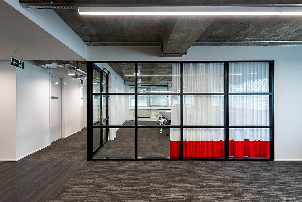 Modern, industrial-style office space with glass walls, exposed ceiling, and red curtains.