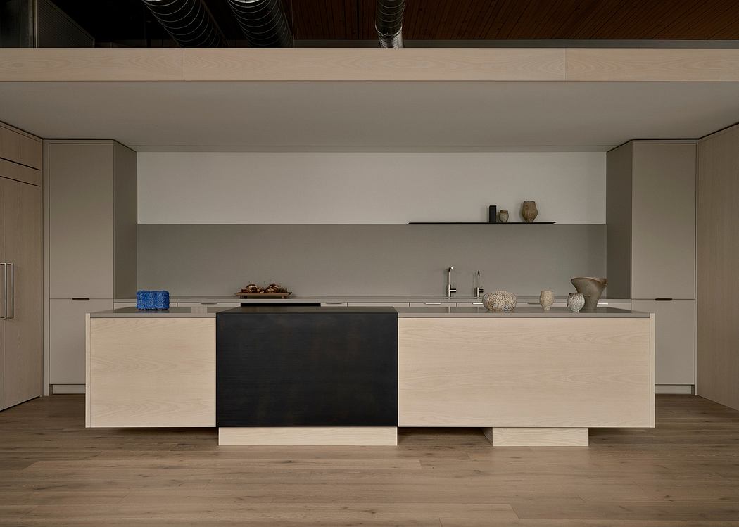 Sleek, minimalist kitchen with light wood cabinetry, black island, and decorative shelving.