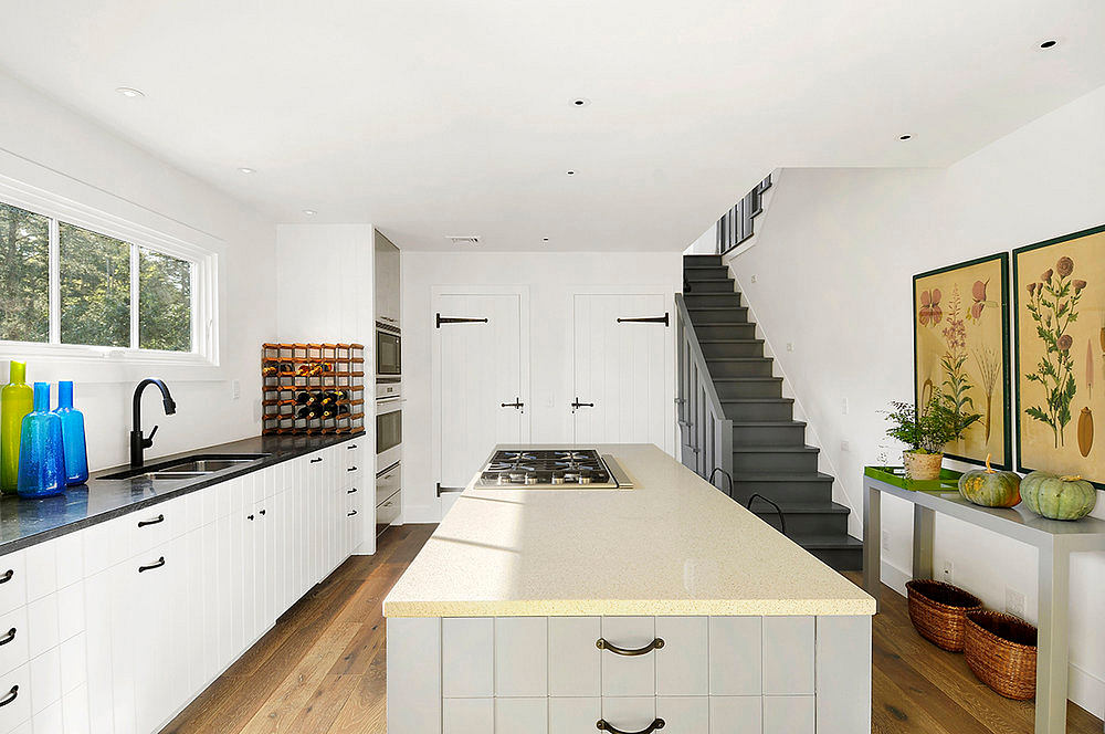 A bright, modern kitchen with a white tile island, cabinetry, and wood floors. Artwork and plants add color.