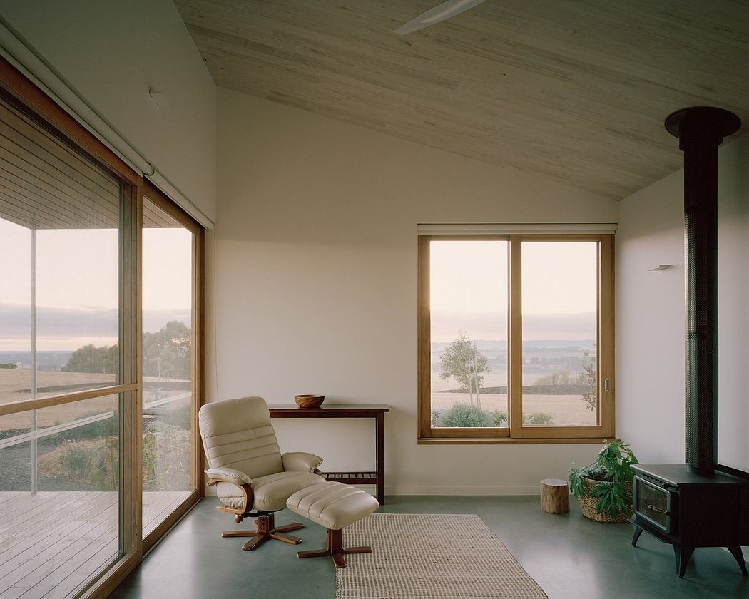 Cozy, minimalist living space with large windows, wooden ceiling, and a comfortable armchair.