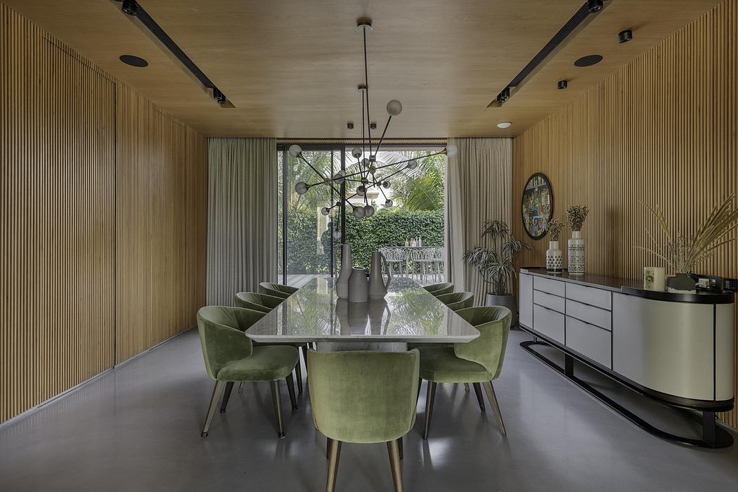 Modern open-concept dining area with wooden slat walls, green velvet chairs, and a striking black chandelier.
