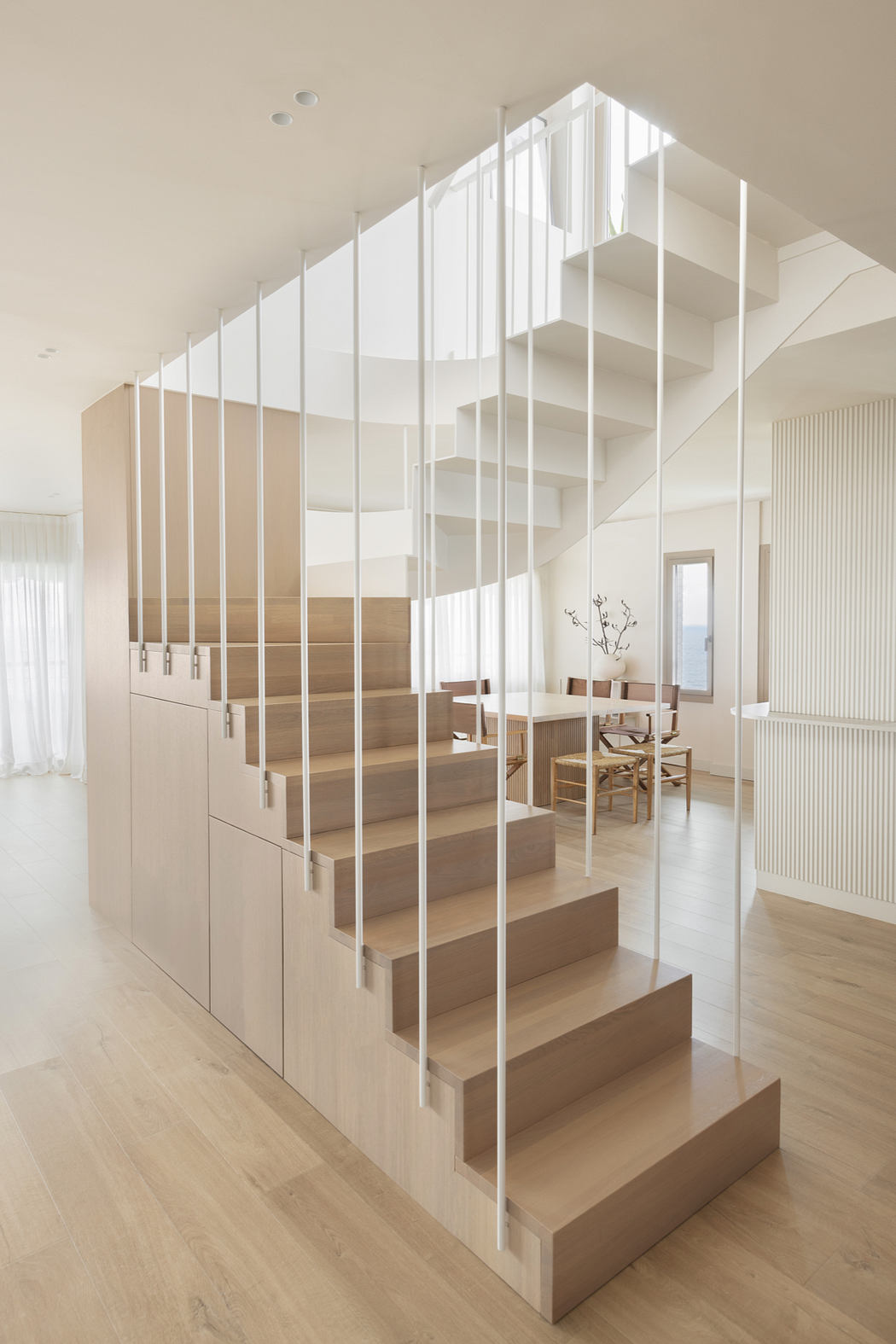 Sleek, minimalist staircase with white metal rails and wooden steps leading to an open dining area.