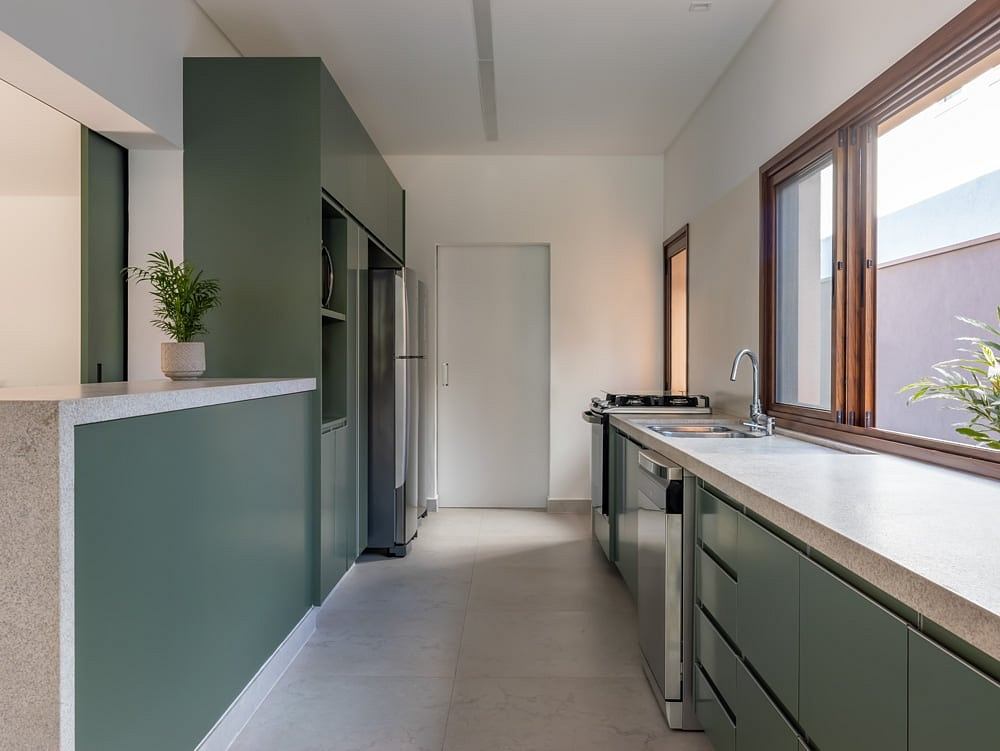 A modern kitchen with green cabinetry, stainless steel appliances, and a large window providing natural light.