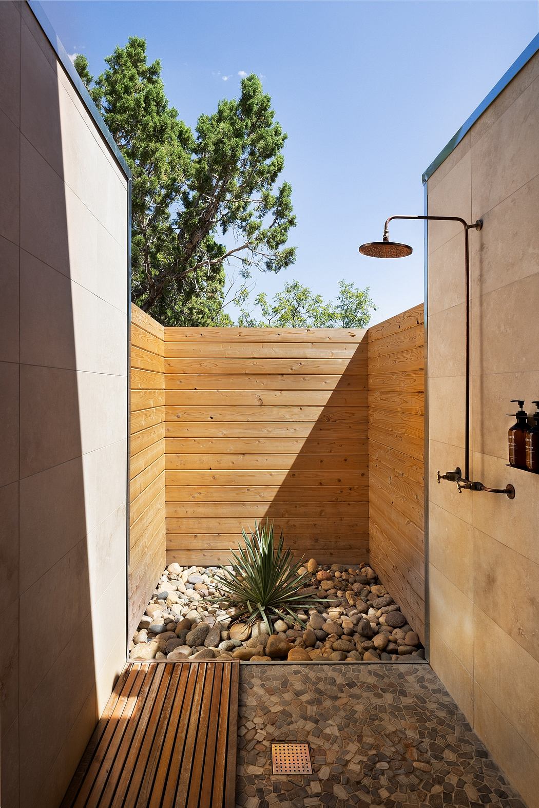 Outdoor shower area with wood paneling, stone flooring, and potted plant.