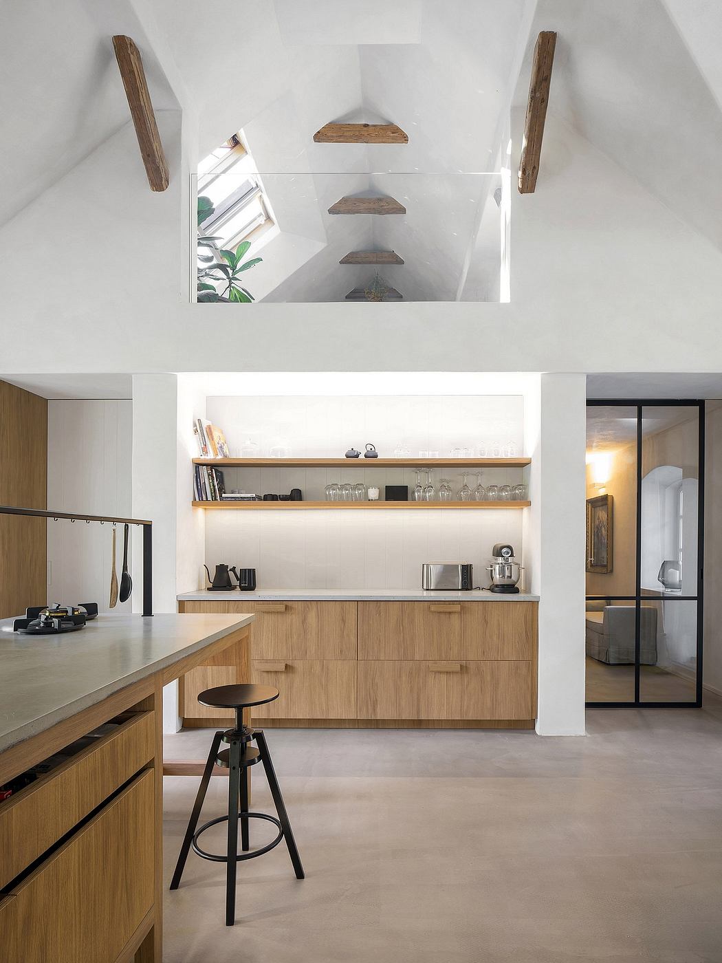 A minimalist, open-concept kitchen with wood cabinetry, floating shelves, and a sleek metal-framed window.