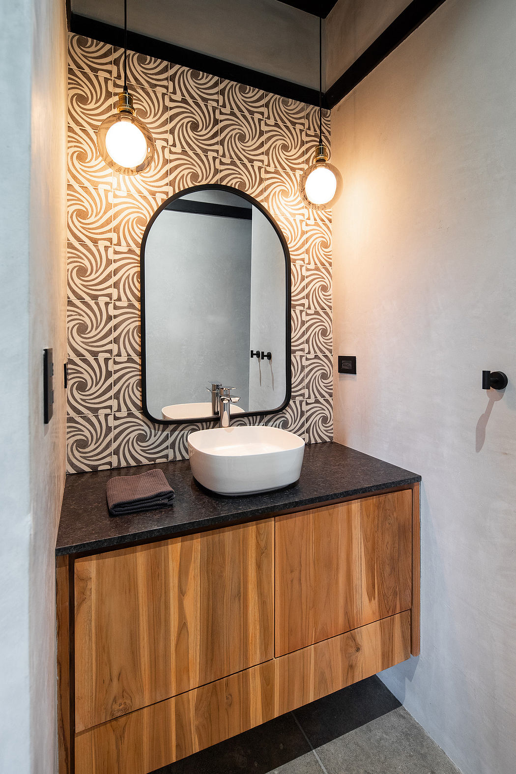 Elegant bathroom with geometric wallpaper, wood vanity, and round mirror.