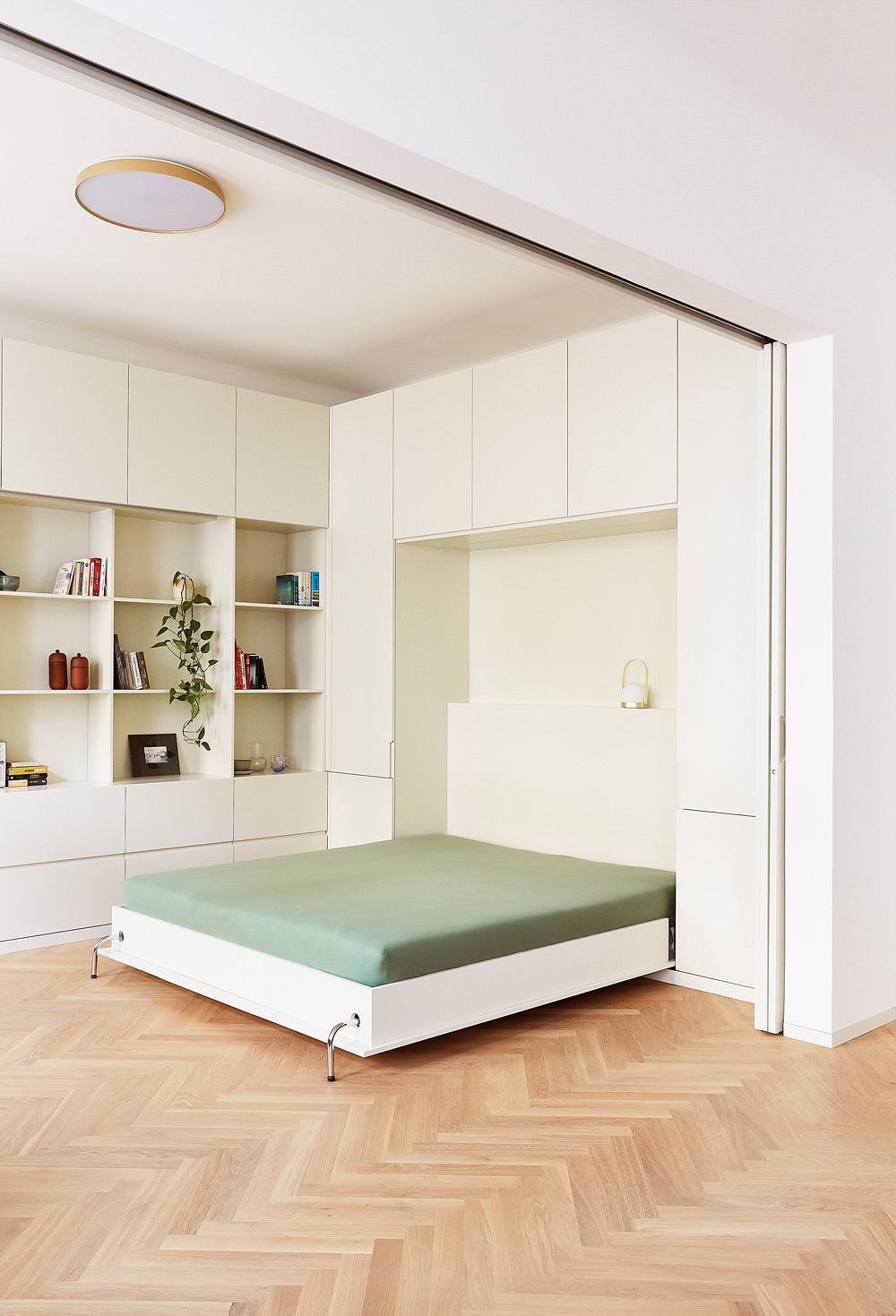 Minimalist bedroom design with built-in cabinetry, floating bed, and herringbone wood flooring.