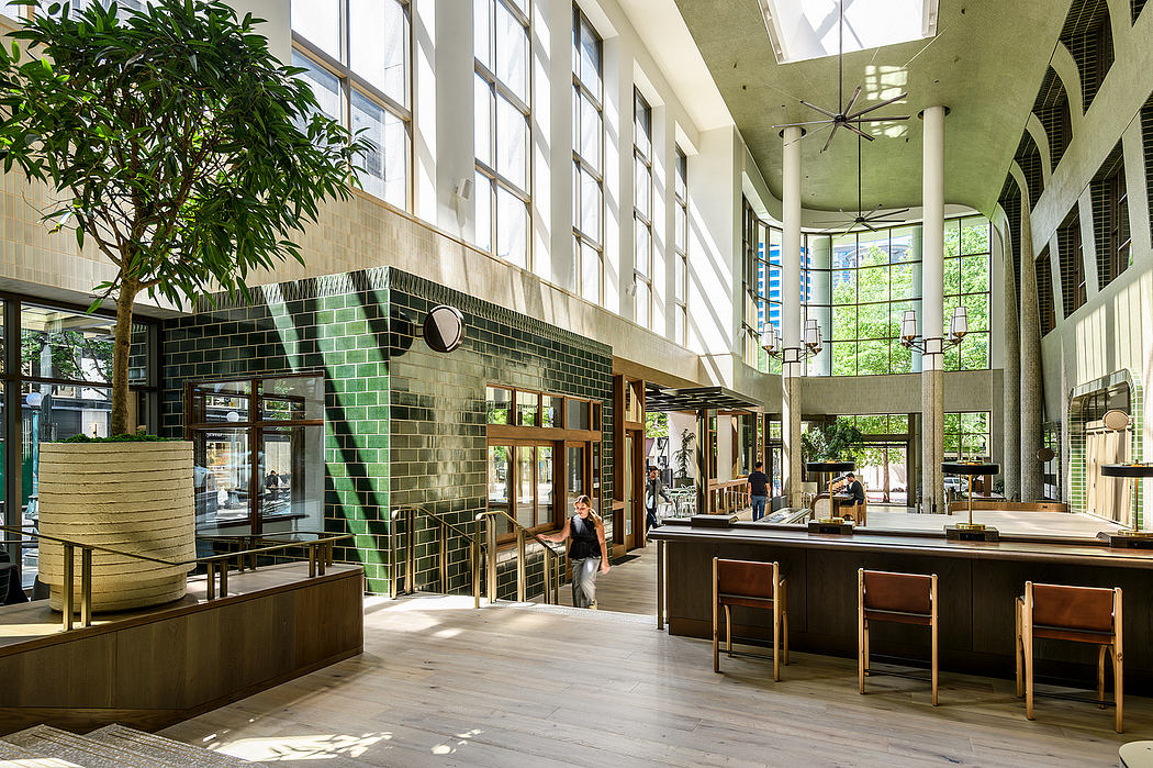 A modern, open-concept lobby with a mix of natural and industrial elements, including large windows, wooden furniture, and a prominent green tile wall.