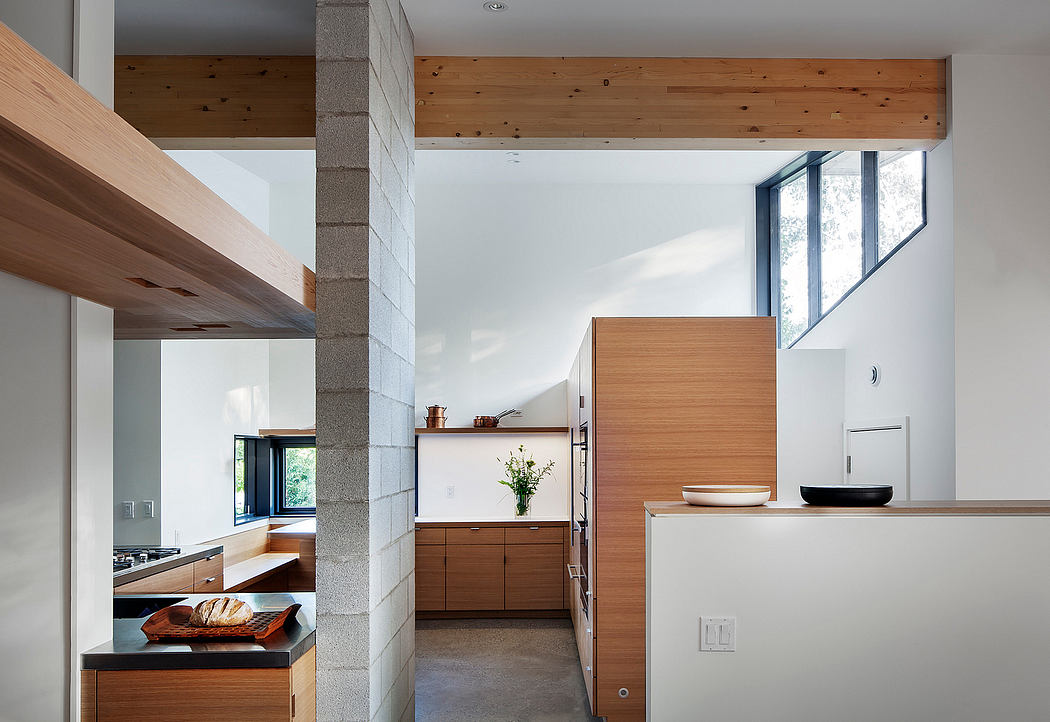 A modern kitchen with wooden cabinetry, stone columns, and large windows providing natural light.