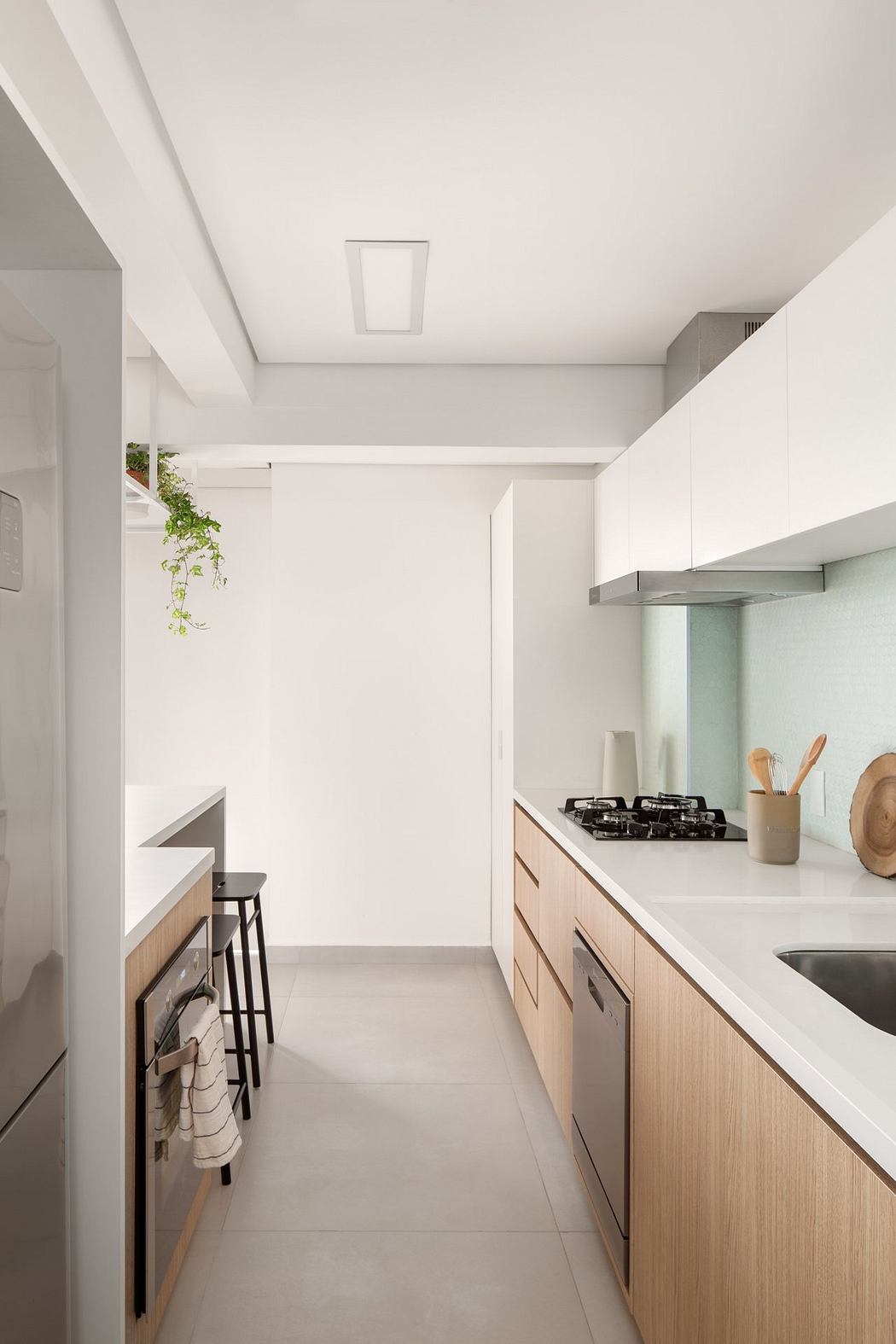 Minimalist kitchen design with sleek white cabinetry, wooden accents, and potted plant.