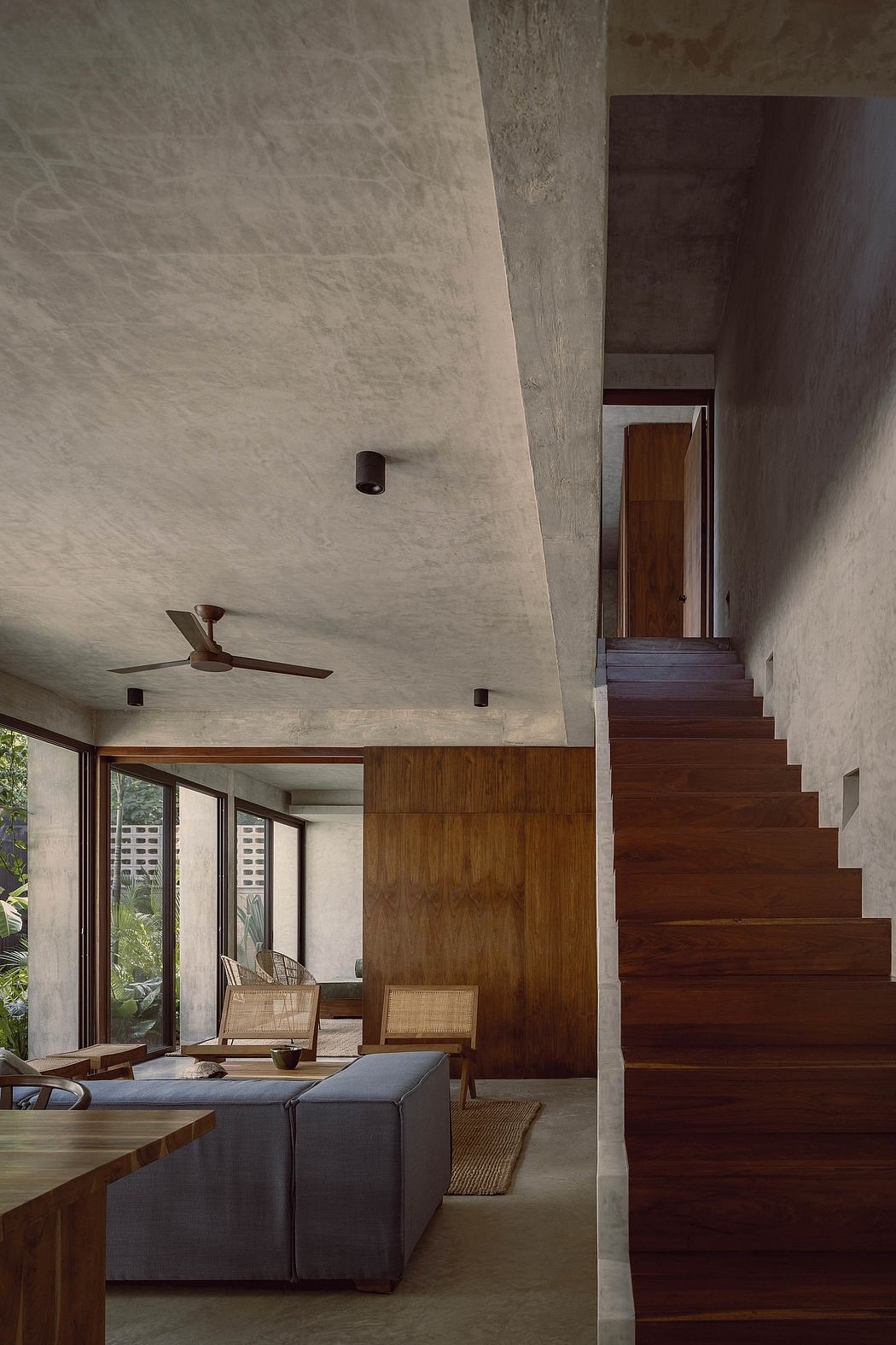 A modern interior with concrete walls, wood paneling, and a striking wooden staircase.