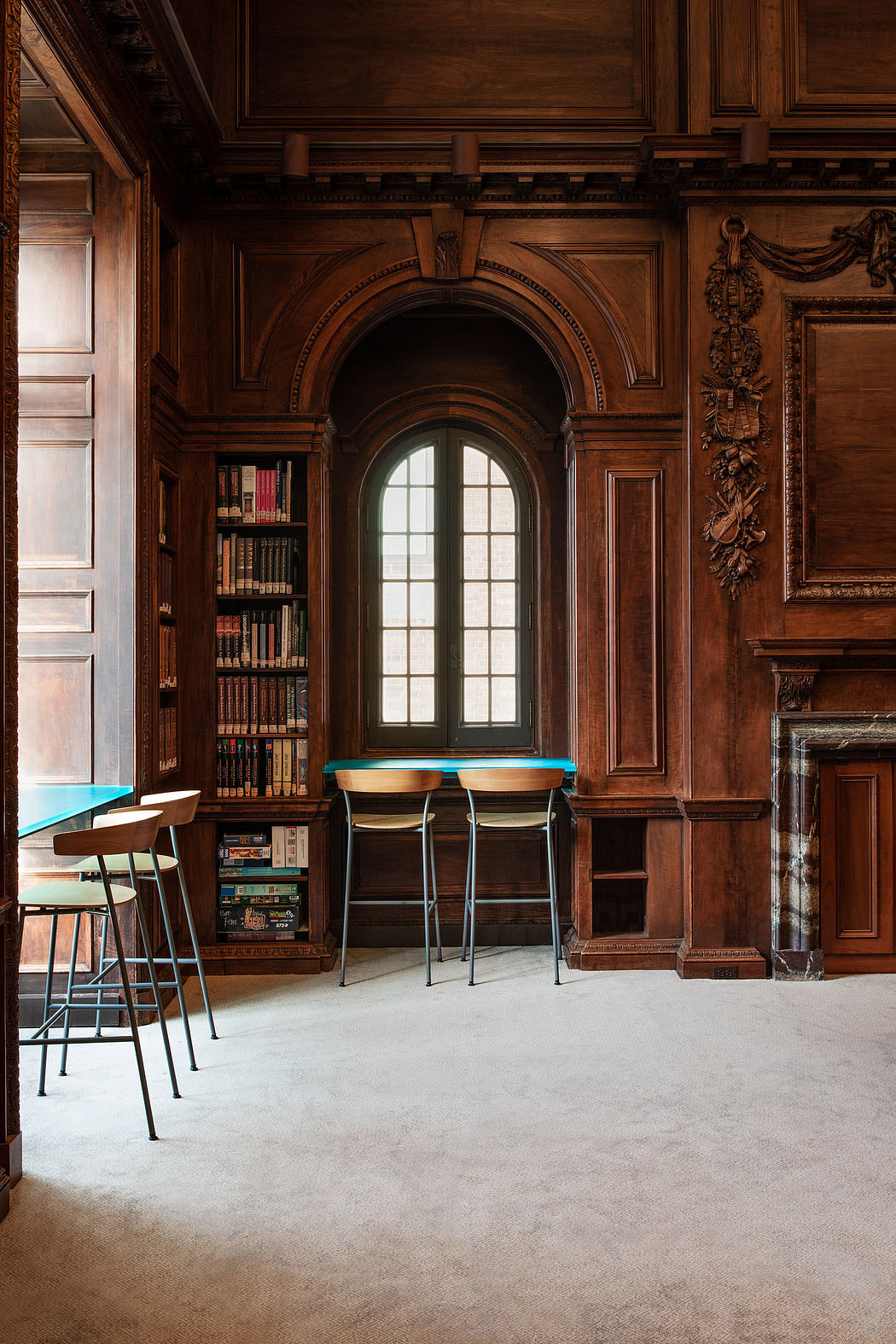 Opulent, wood-paneled library with arched windows, ornate bookshelves, and modern bar stools.