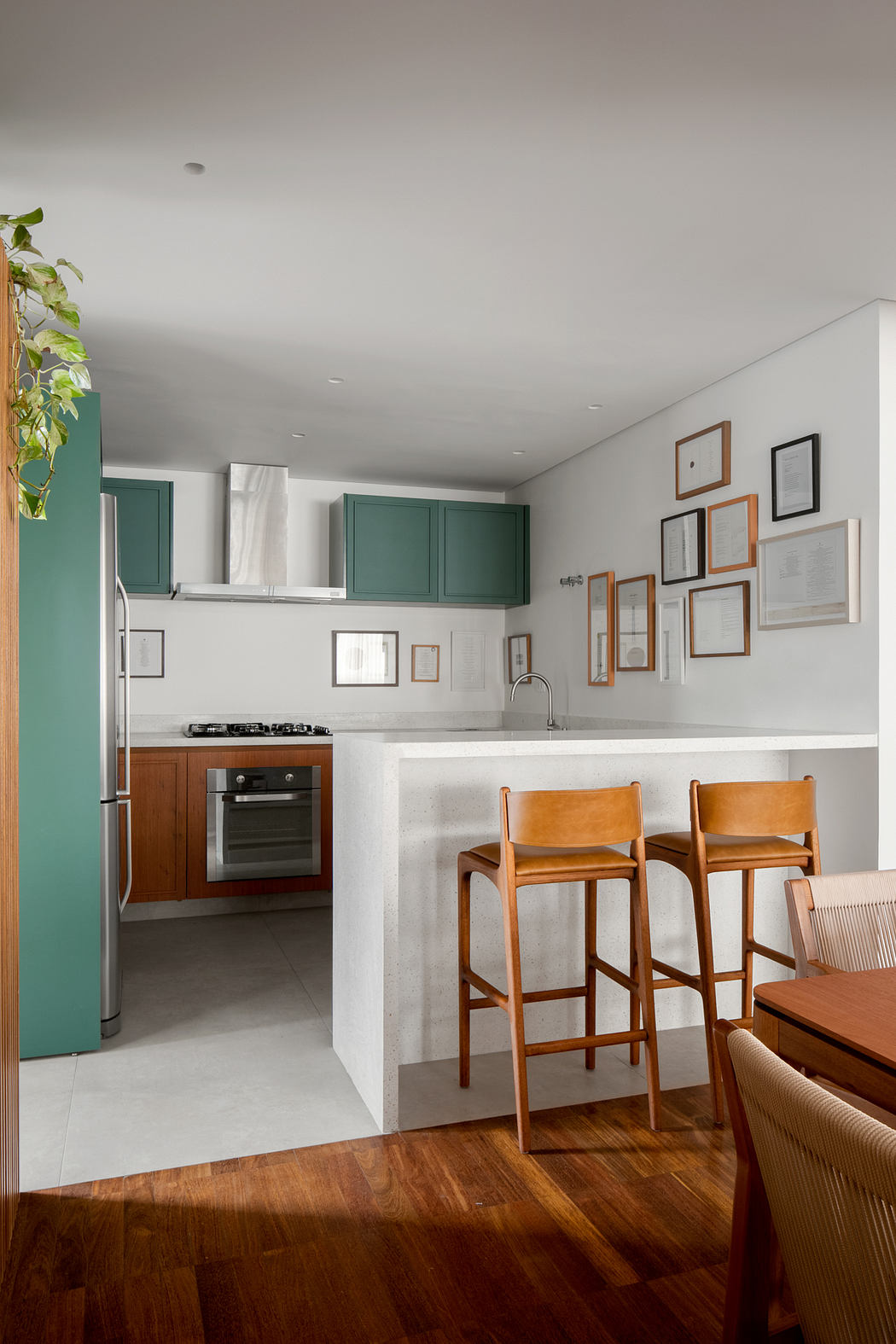 A modern kitchen with white walls, green cabinets, and wood floors, featuring a gallery wall and bar stools.