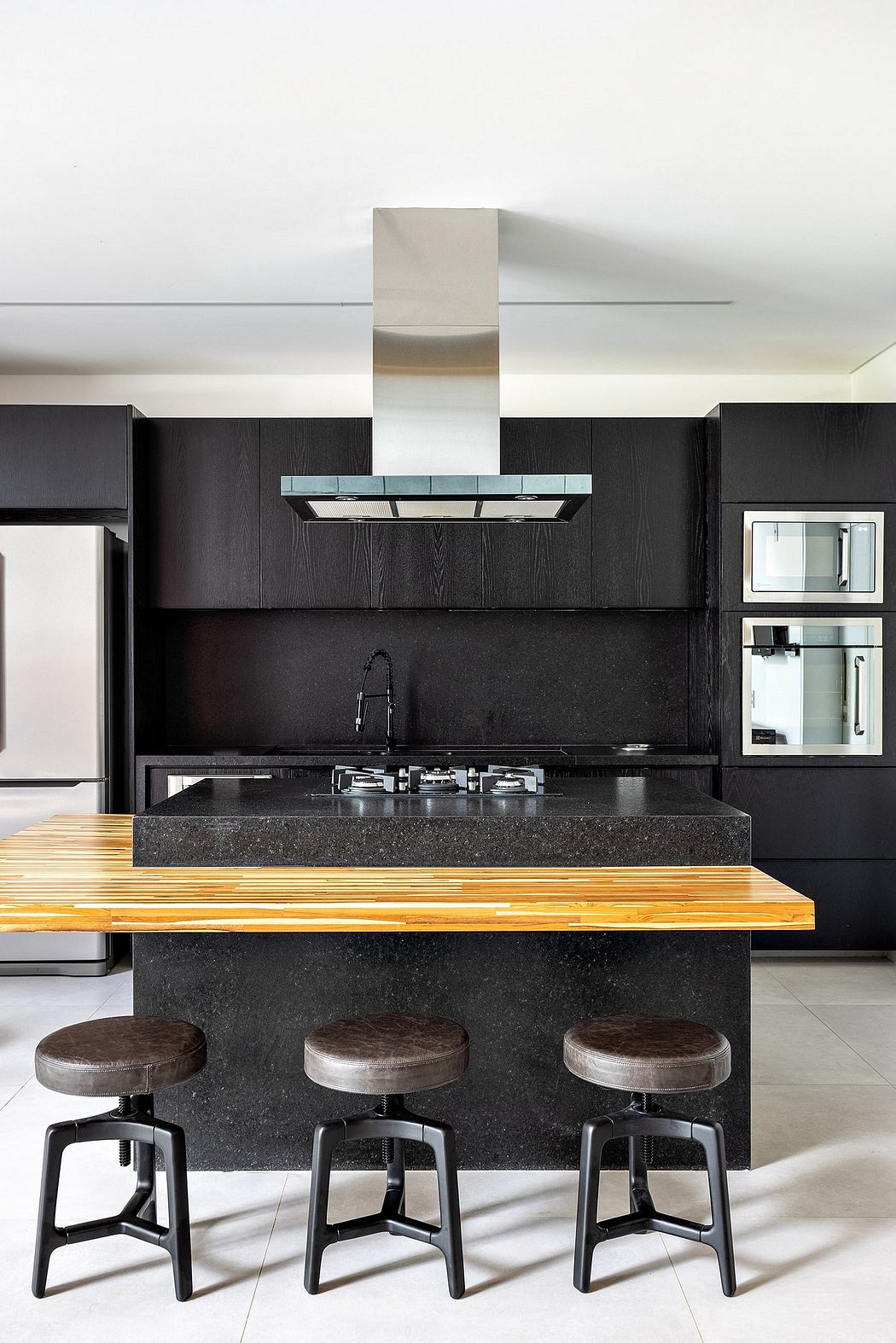 Modern kitchen with sleek black cabinets, granite countertop, and wooden bar stools.
