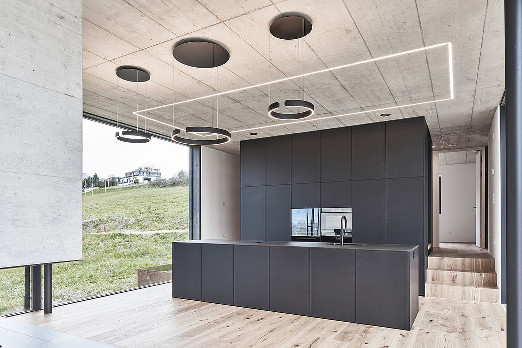 Modern kitchen with sleek black cabinetry, minimalist lighting fixtures, and panoramic windows overlooking a grassy landscape.