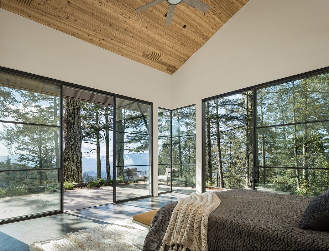 Spacious bedroom with wooden ceiling, floor-to-ceiling windows, and forest view.