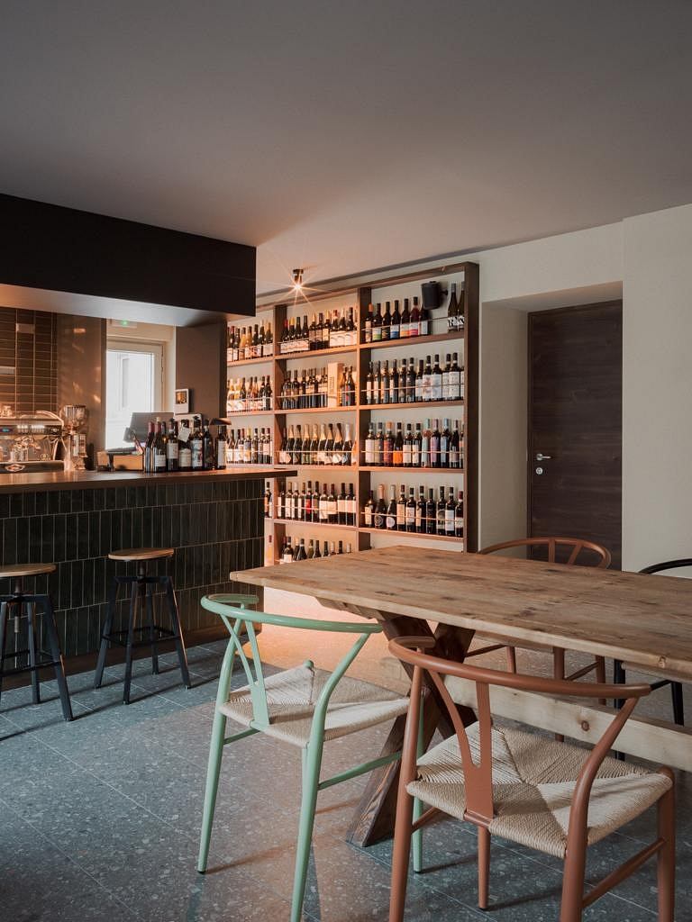 A cozy and stylish wine bar with wooden furnishings, shelves stocked with bottles, and a rustic aesthetic.