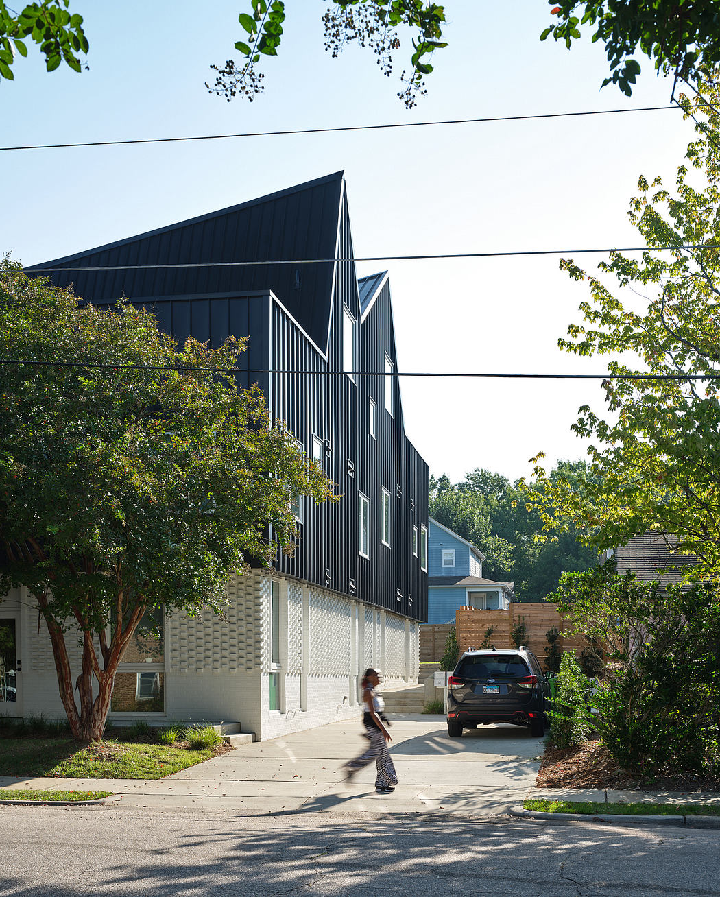 Angular black metal facade with layered patterns contrasting the surrounding greenery.