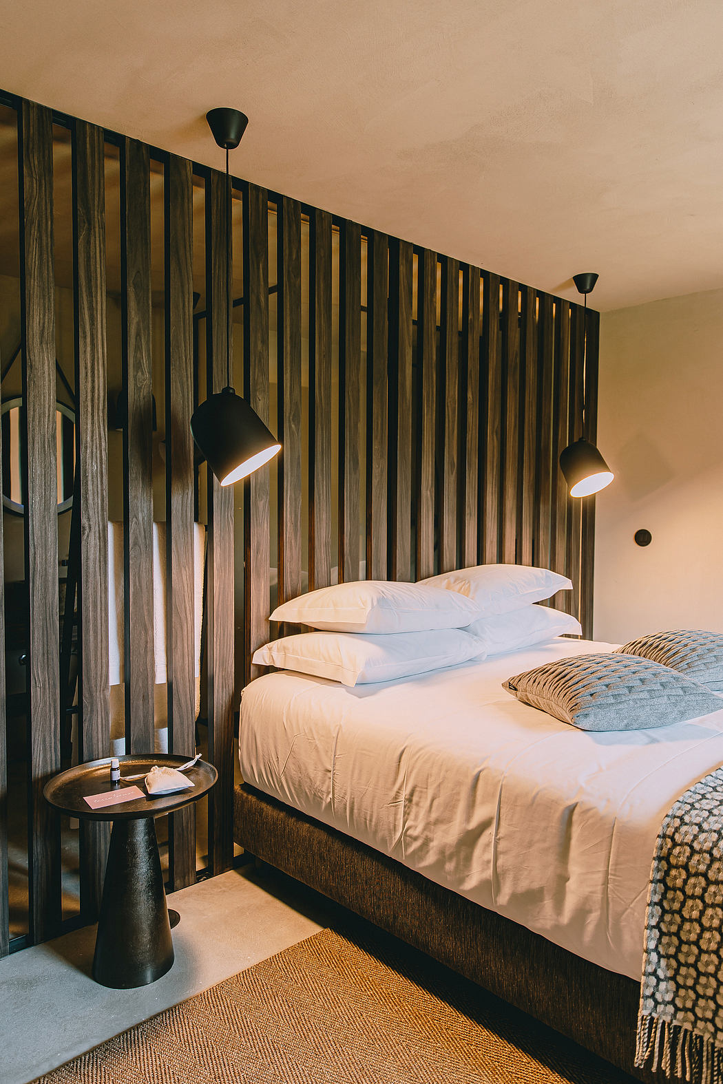 A rustic and cozy bedroom with a wooden paneled wall, pendant lights, and textured bedding.