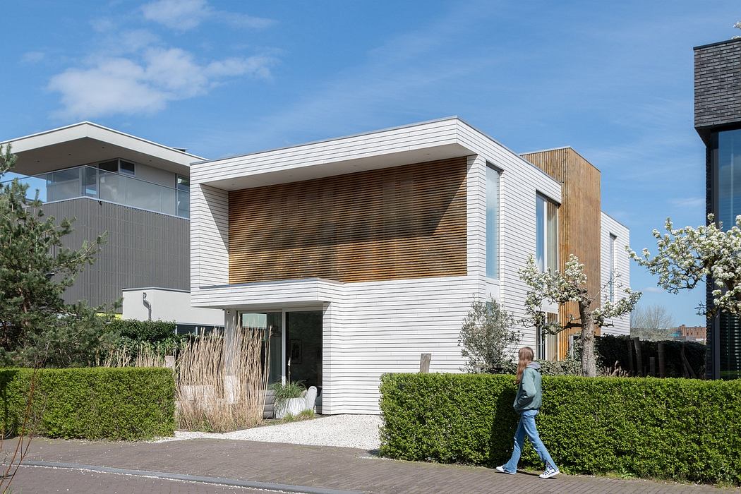 Modern white facade with wooden accents, surrounded by landscaping and a person in foreground.