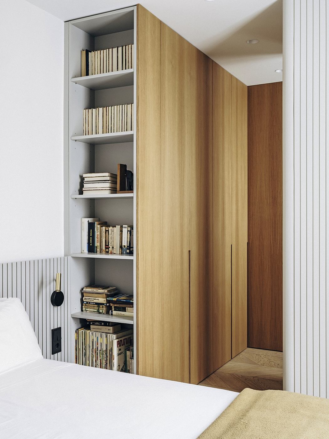 A minimalist bedroom with wooden storage cabinets and shelves displaying books.