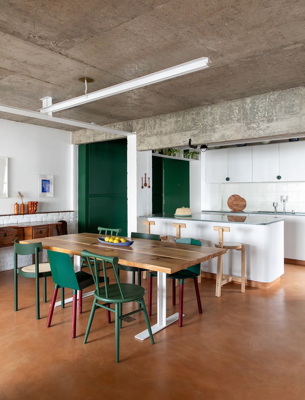 A modern kitchen with exposed concrete walls, wooden dining table, and green accents.