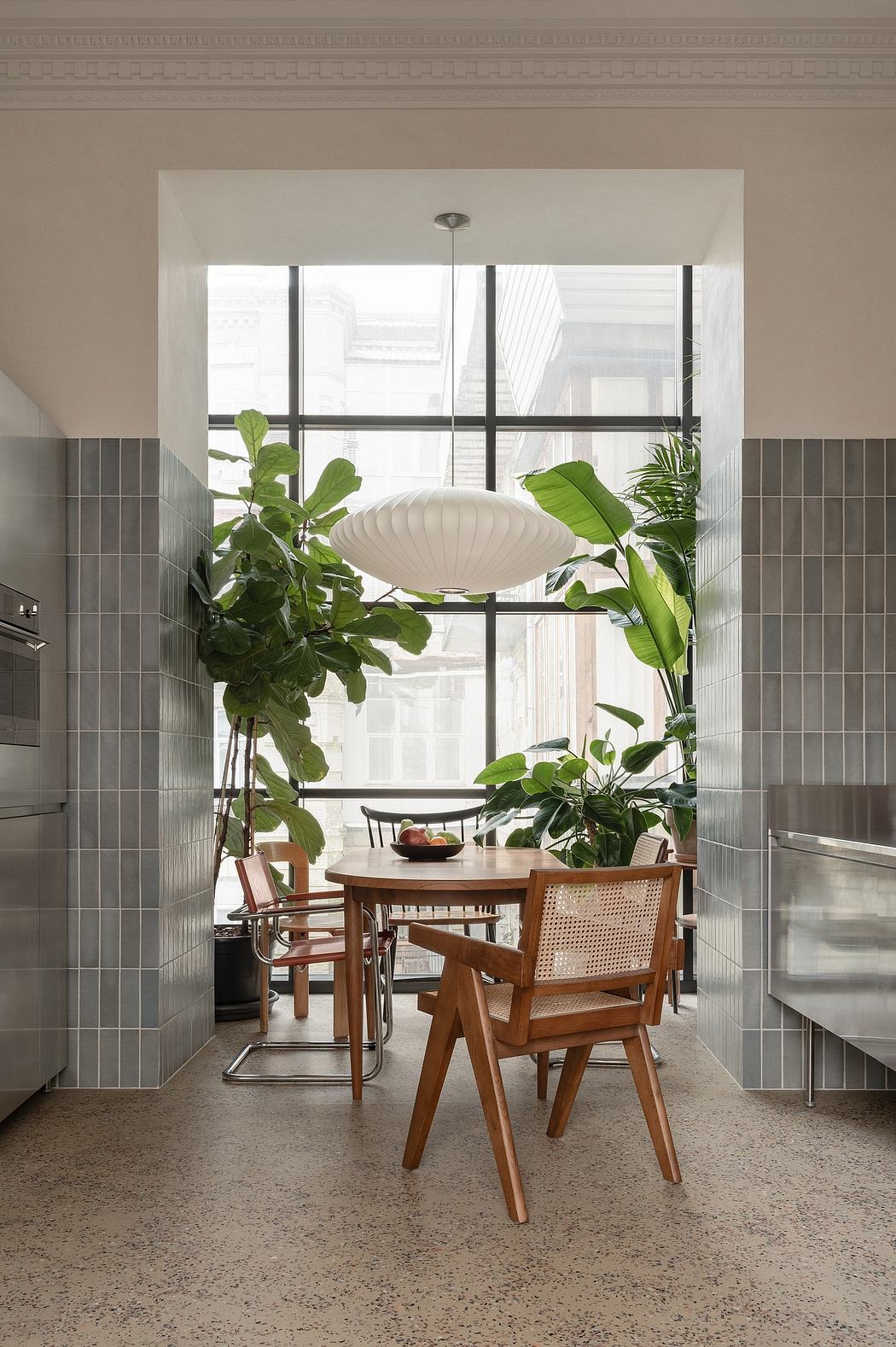 A modern kitchen with large windows, tropical plants, and a mid-century dining set.