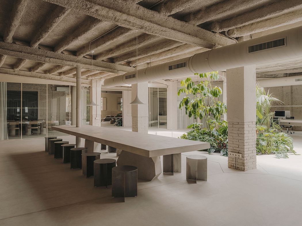 An open-concept office space with exposed concrete ceilings, natural light, and lush greenery.