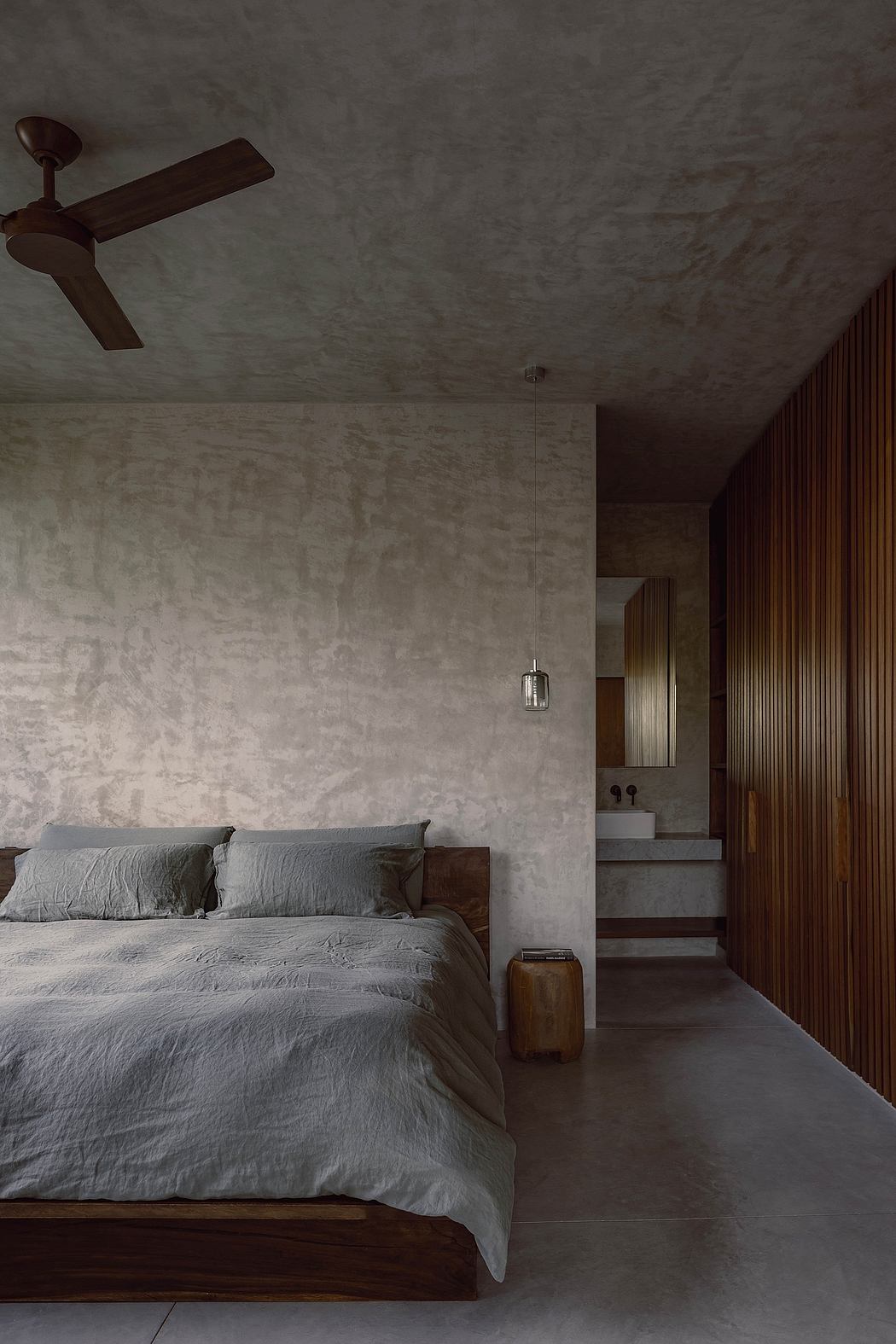 Moody, minimalist bedroom with concrete walls, wooden accents, and a suspended ceiling fan.