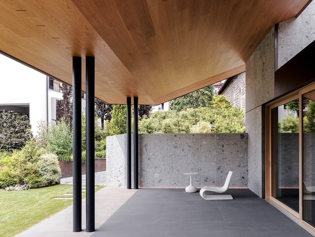 Minimalist exterior with concrete walls, wood ceiling, and sliding glass doors overlooking lush greenery.