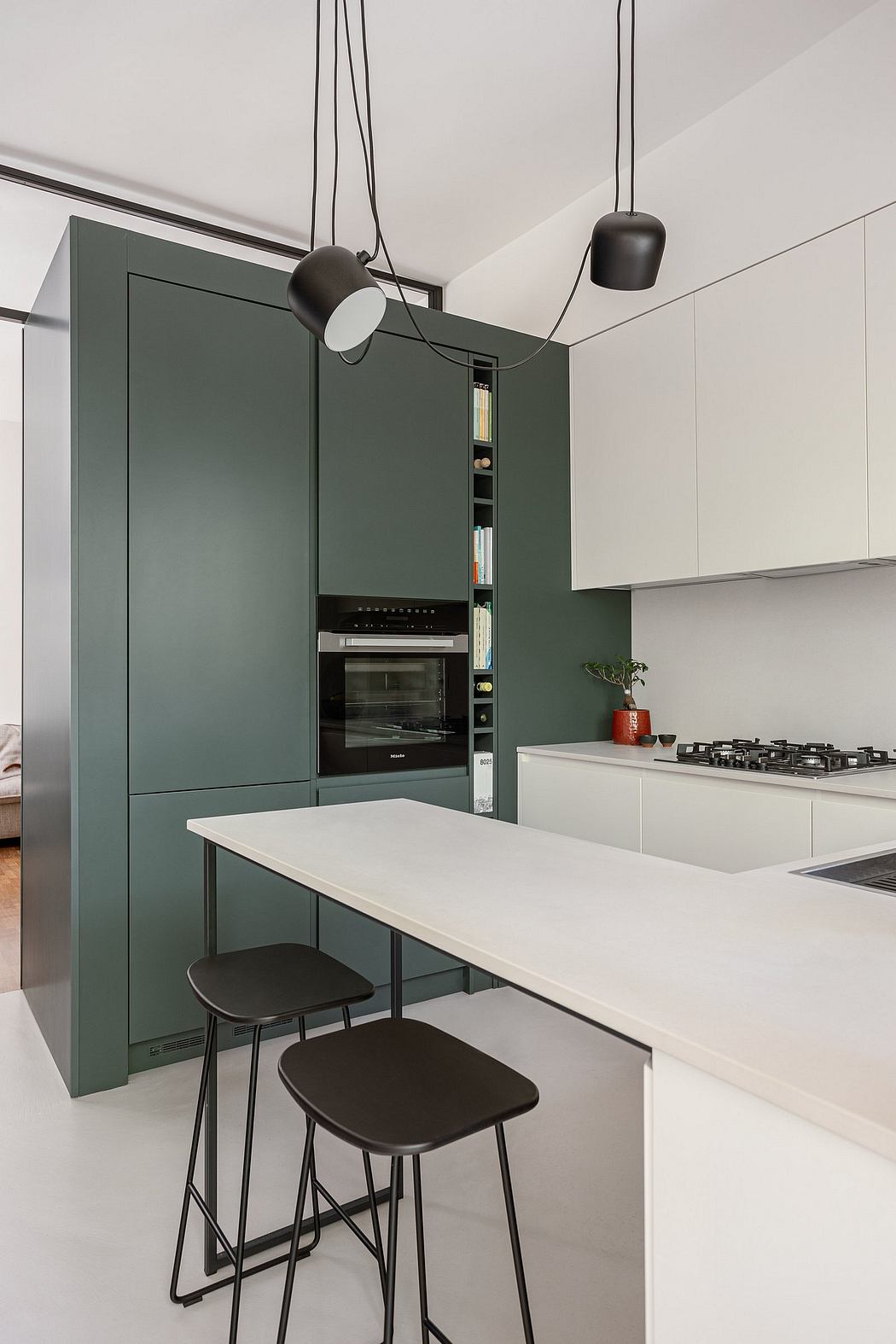 A modern kitchen with sleek green cabinets, white countertops, and black pendant lights.