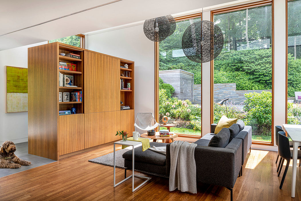 Spacious modern living room with wood paneling, pendant lights, and views of lush greenery.