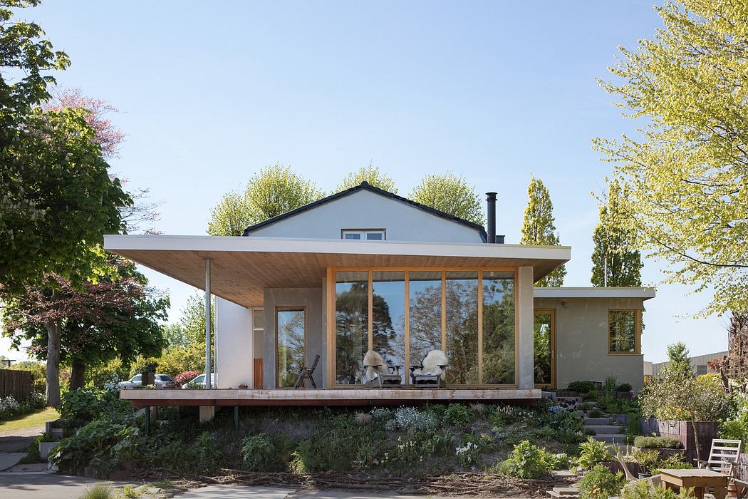 A modern, single-story home with a large, covered deck and expansive windows overlooking a lush garden.