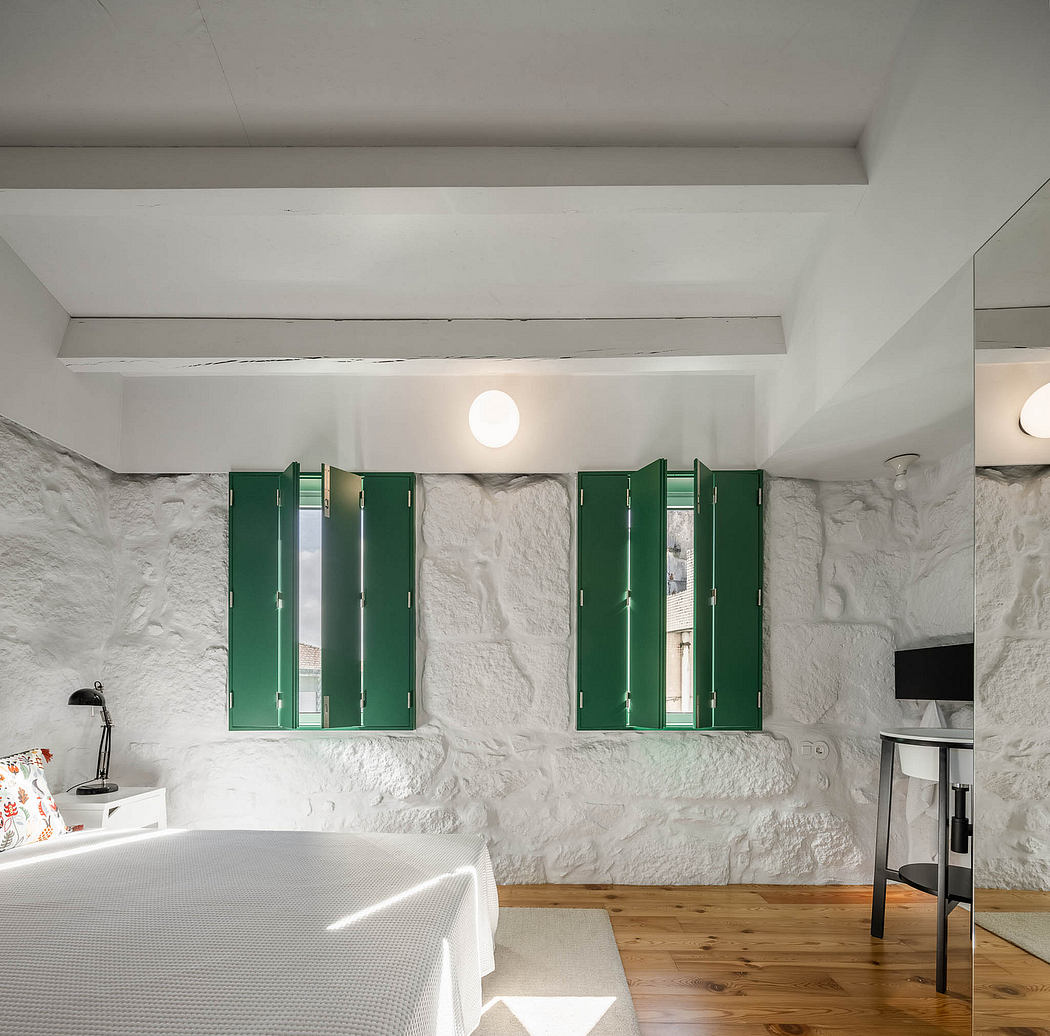 A minimalist bedroom with white plaster walls, green shutters, and a wooden floor.
