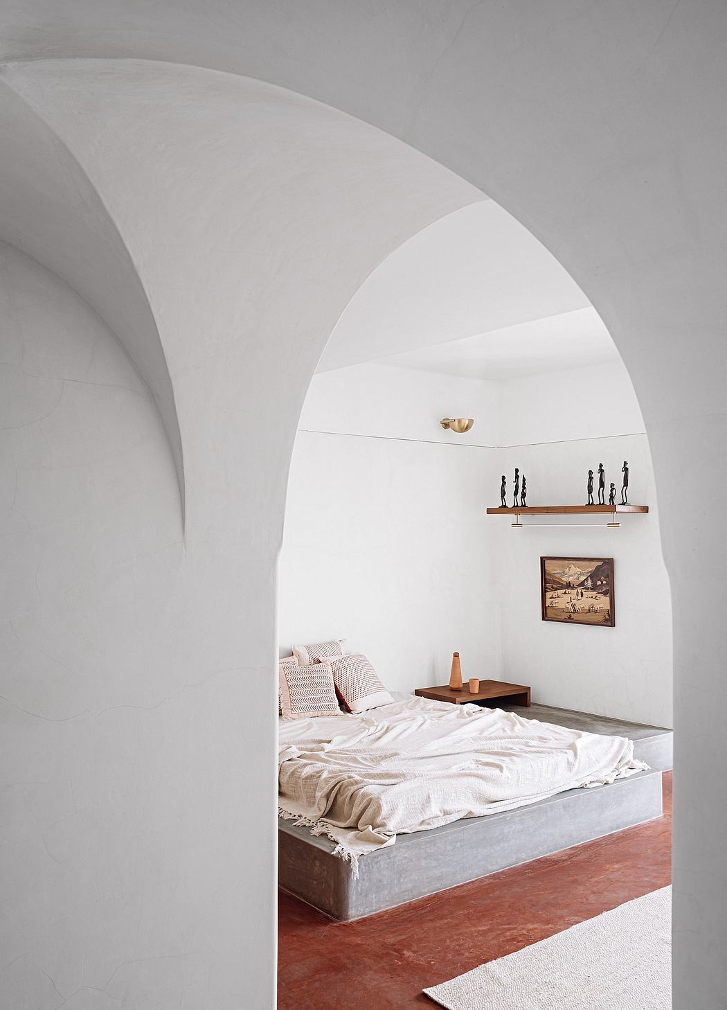 Arched, minimalist bedroom with concrete platform bed, wooden accents, and sculptural wall art.