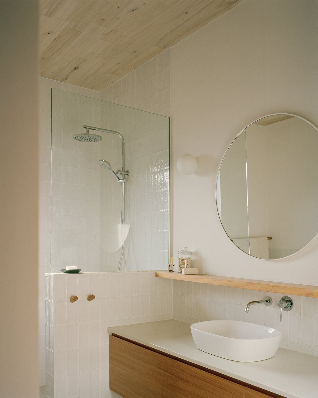 A sleek, minimalist bathroom with a wooden vanity, round mirror, and rainfall shower.