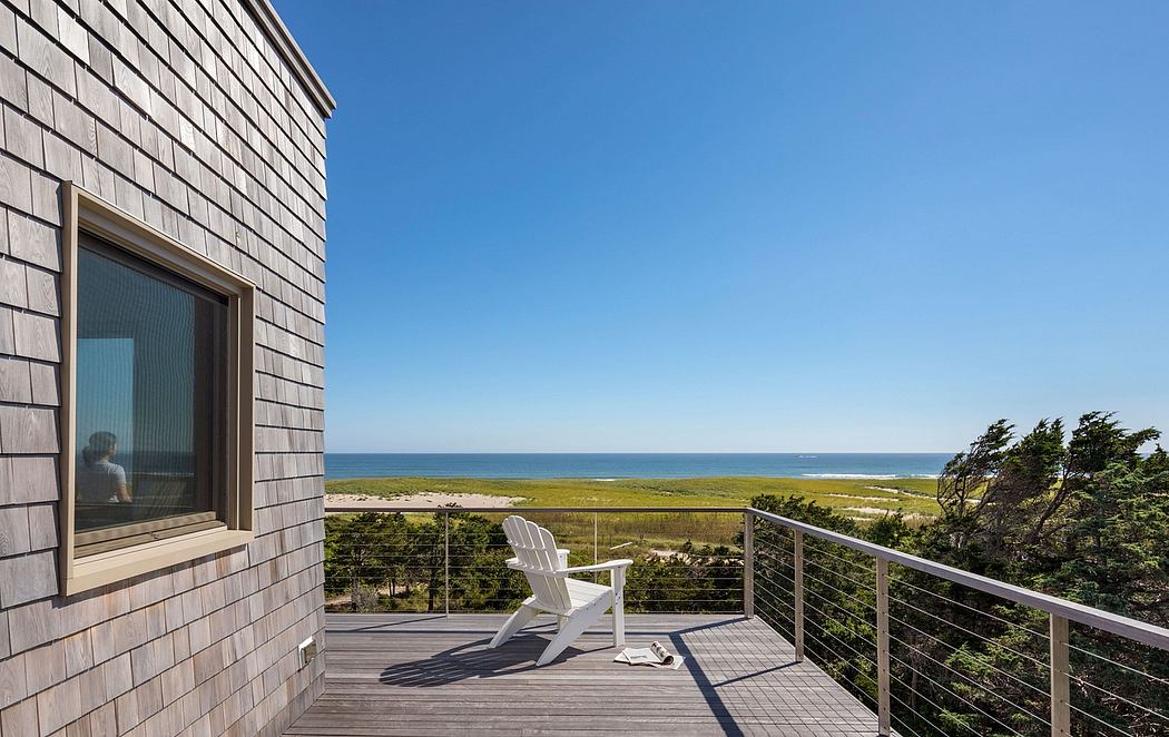 Wooden shingle-clad exterior with expansive beach views and an elevated deck with Adirondack chair.