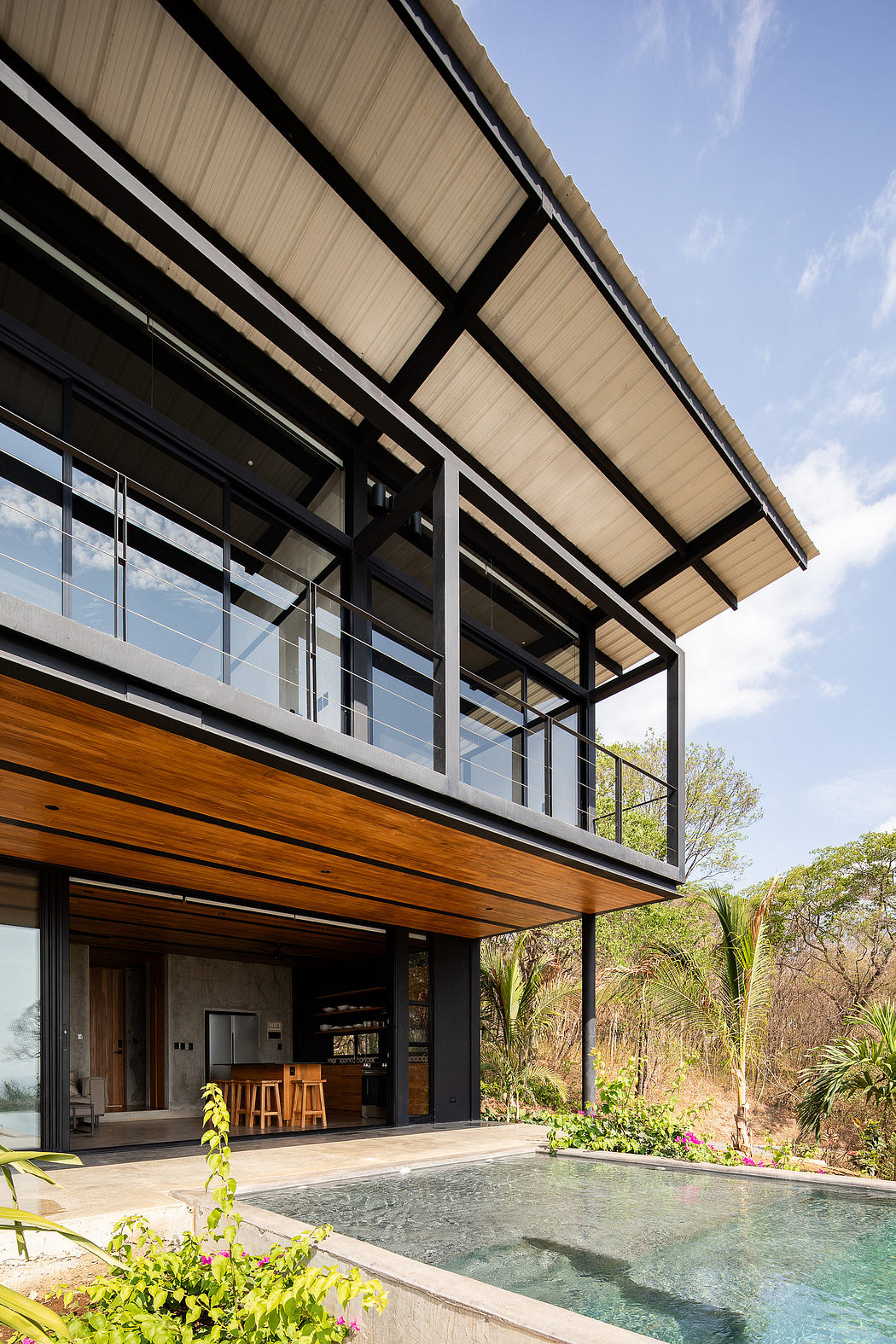 Modern architectural design with wooden accents, glass panels, and a swimming pool set against lush foliage.