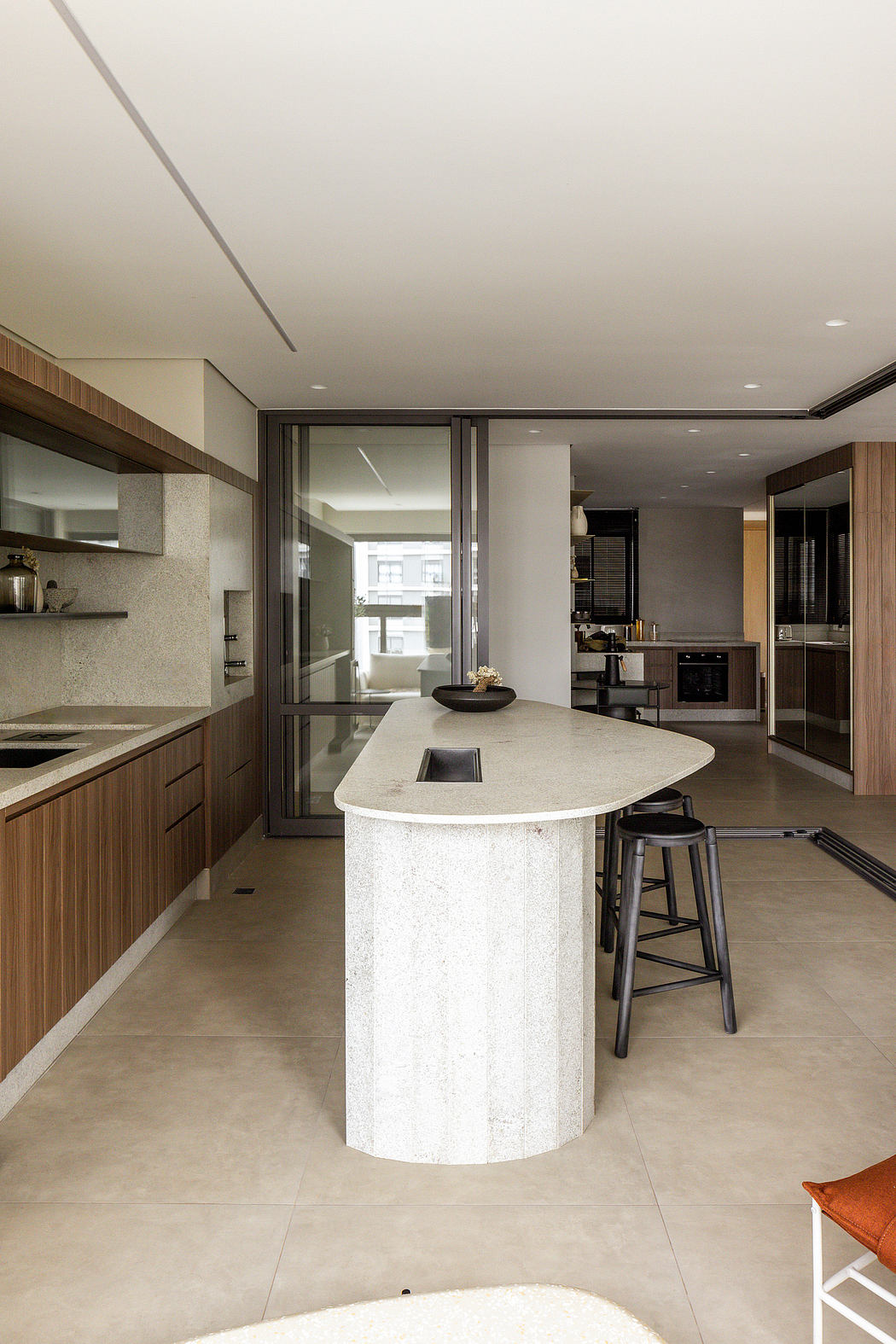 Sleek modern kitchen with curved marble island, wood cabinetry, and large windows.